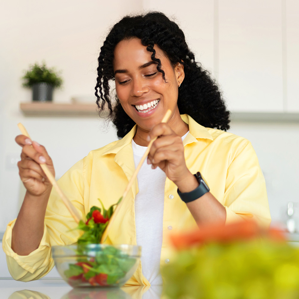 Na imagem, uma mulher negra prepara uma salada