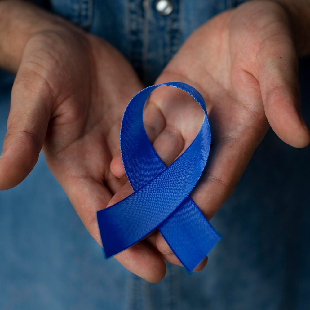 Na imagem, duas mãoes seguram o laço de cor azul, sómbolo da campanha para prevenção ao câncer de próstata no Novembro Azul