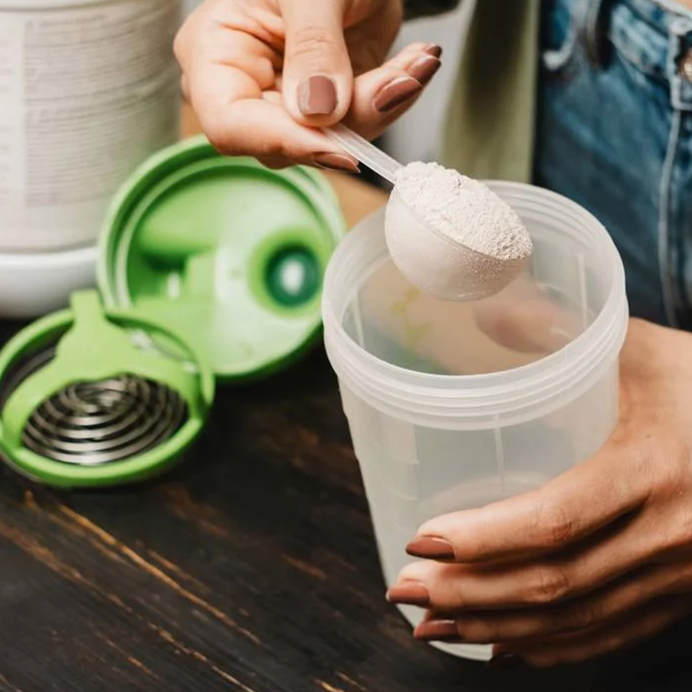 Na imagem, uma pessoa prepara um shake adicionando de proteína em pó