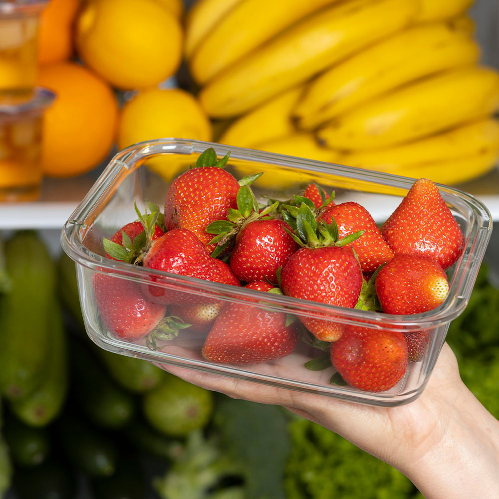 Na imagem, um pote com morangos em foco, ao redor outras frutas como banana e laranja