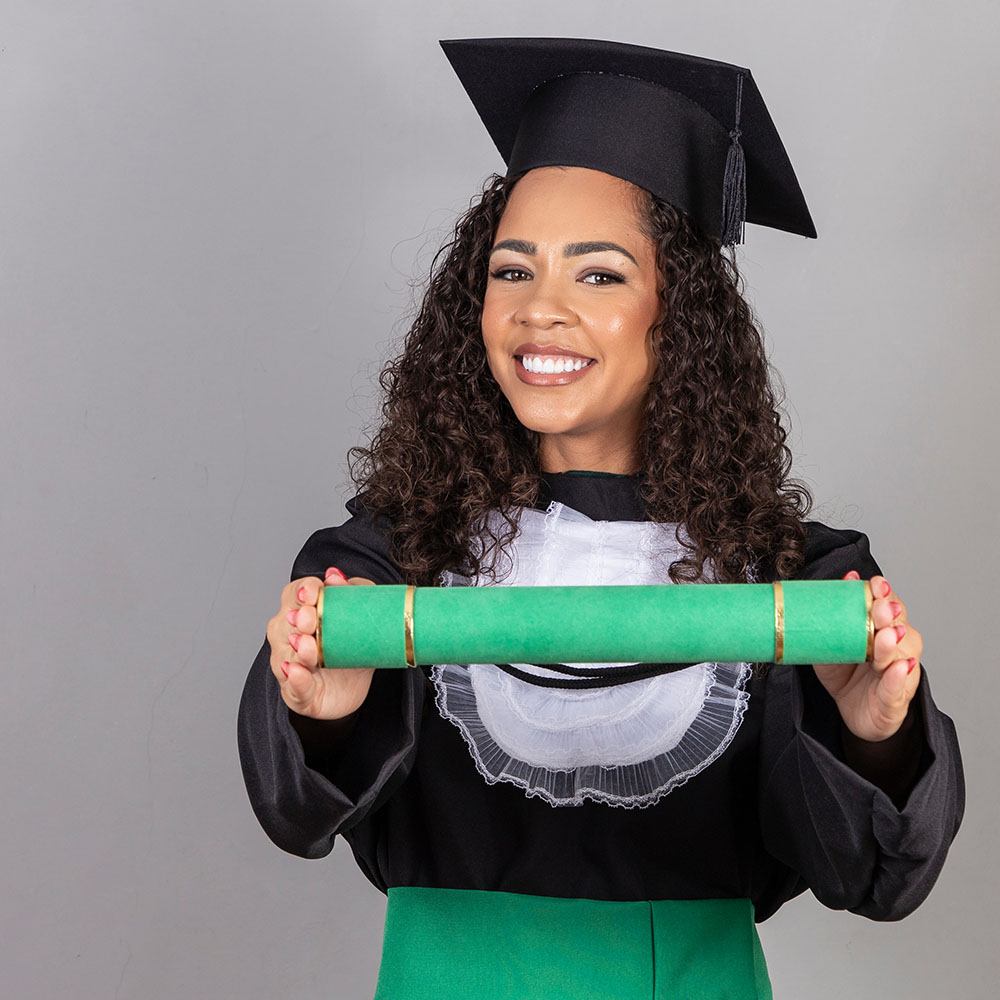 Na imagem, uma mulher, trajada com beca e capelo, sorri para a foto segurando seu canudo de formatura