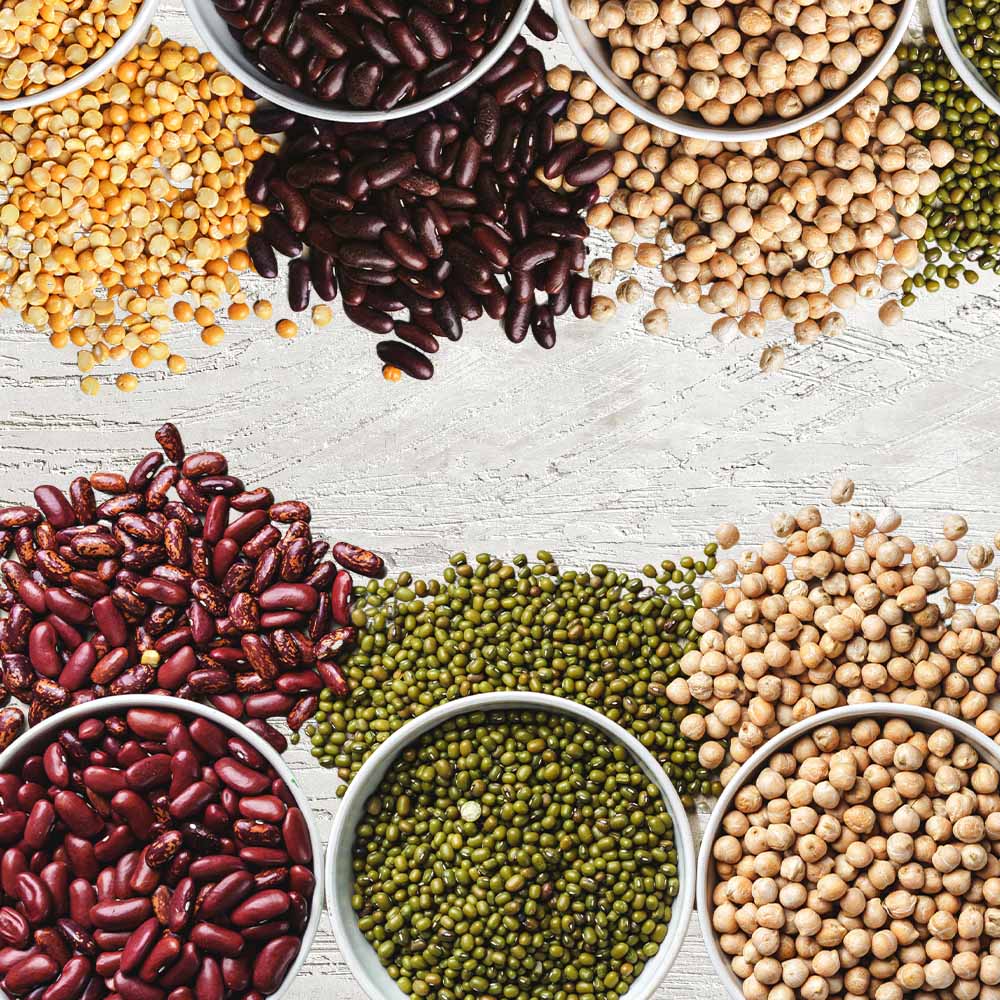 Na imagem estão dispostas lado a lado porções de feijão, grão-de-bico e lentilha, como exemplos de alimentos do grupo das leguminosas