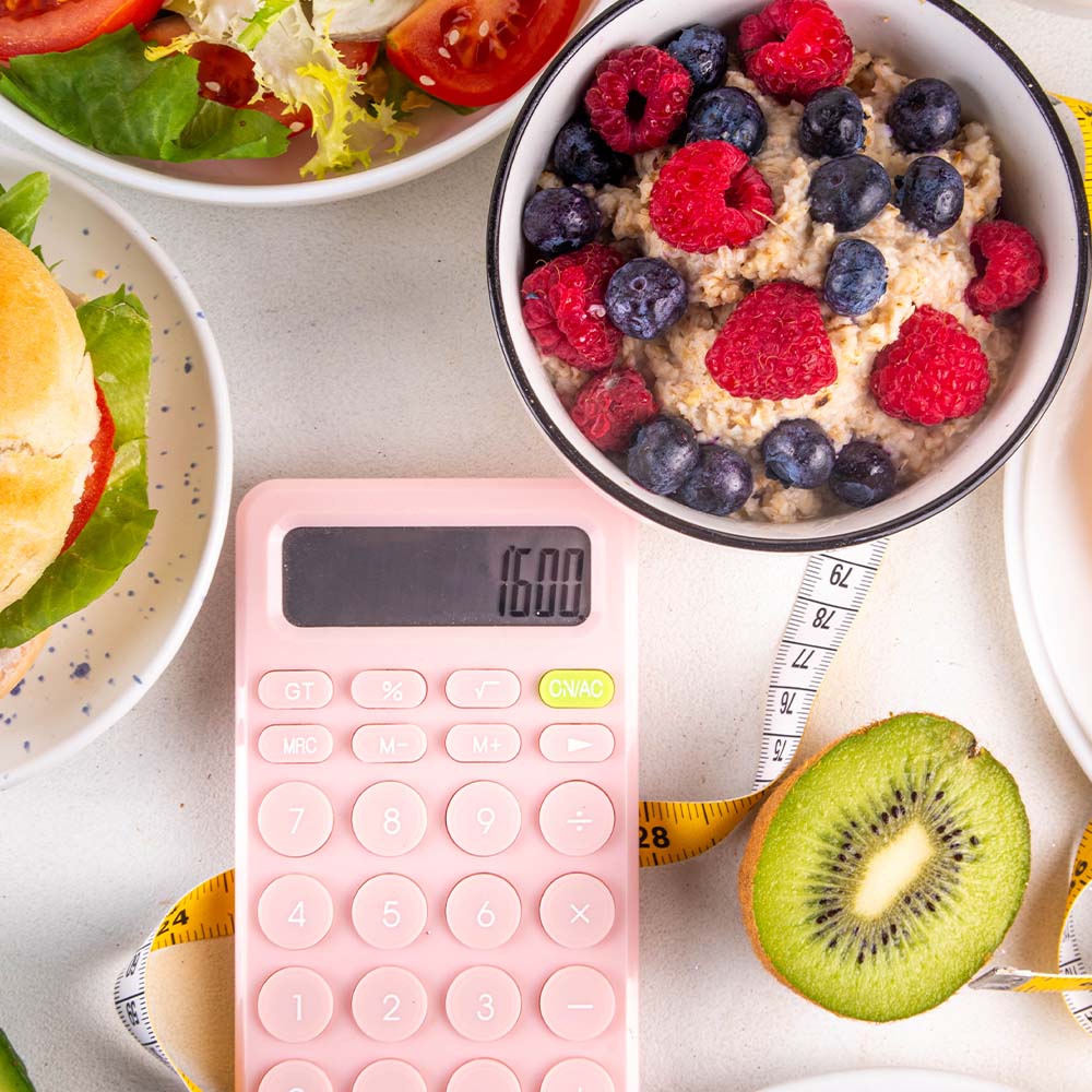 Na foto, estão alguns pratos de refeições e no meio uma calculadora representando o cálculo de calorias