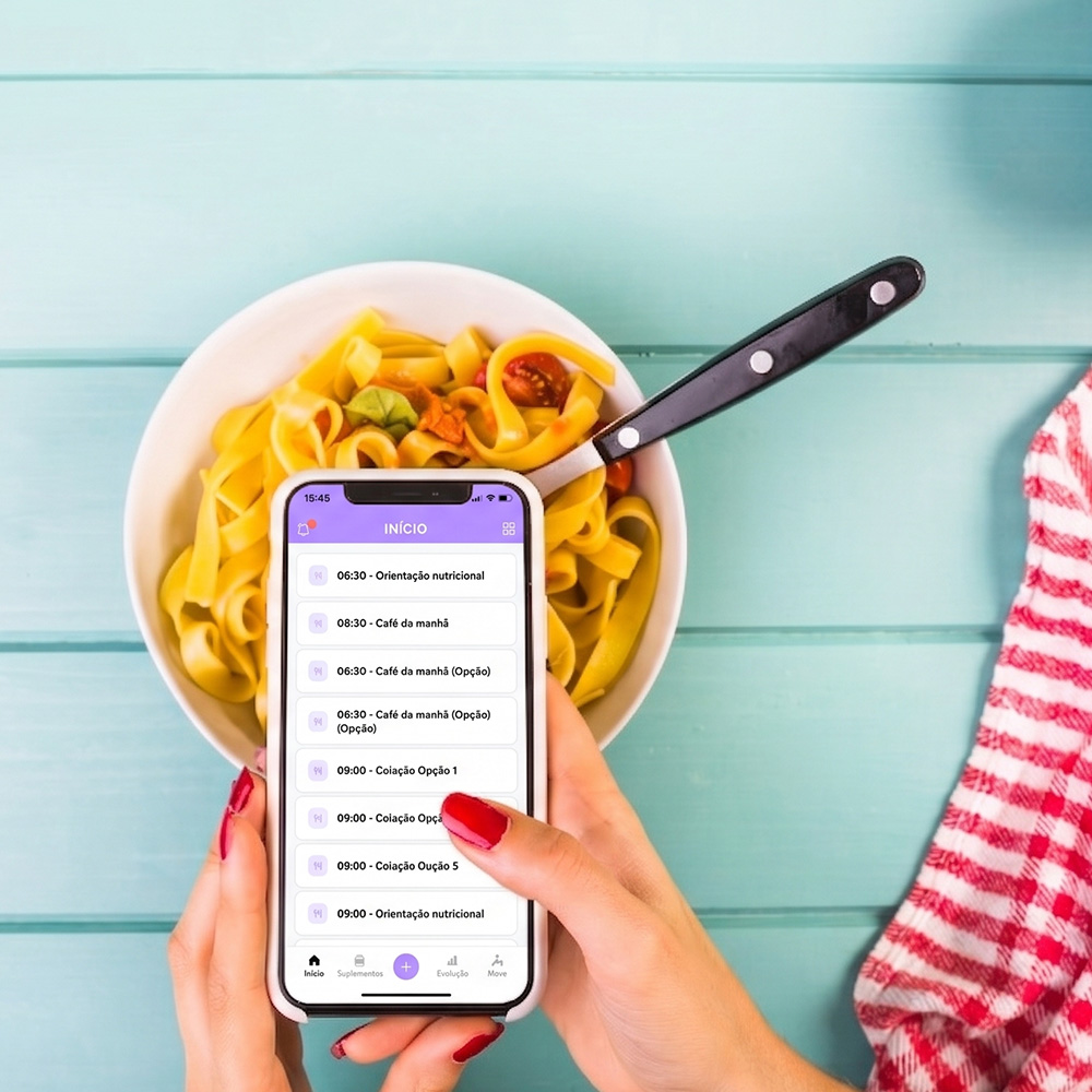 Na imagem, um celular com o aplicativo do webdiet para pacientes aberto e ao fundo um prato de macarrão.