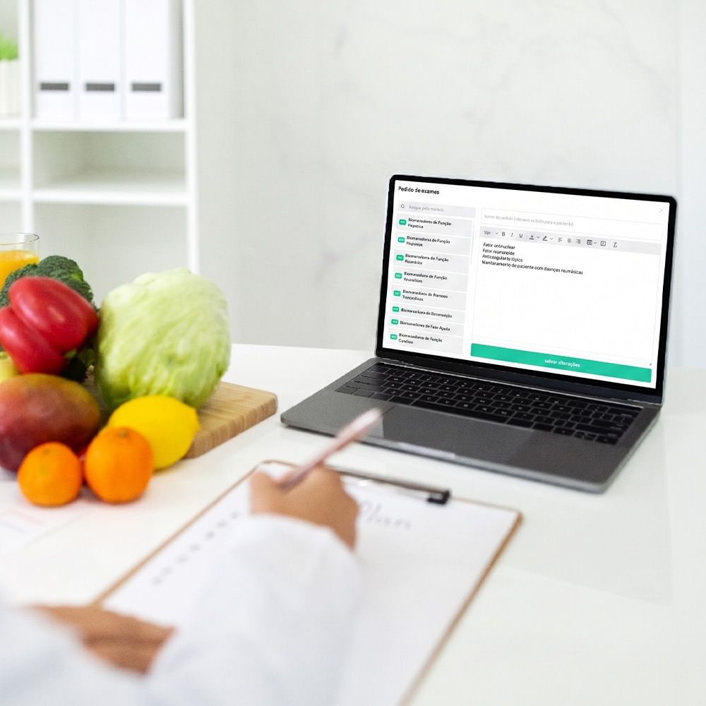 Na foto, um computador com a tela do webdiet logada e uma pessoa fazendo anotações.
