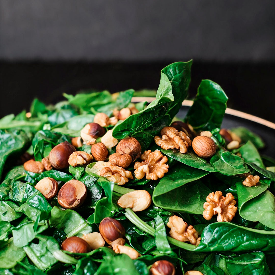 Salada de folhas verdes frescas coberta com nozes e avelãs inteiras em um prato sobre fundo escuro.